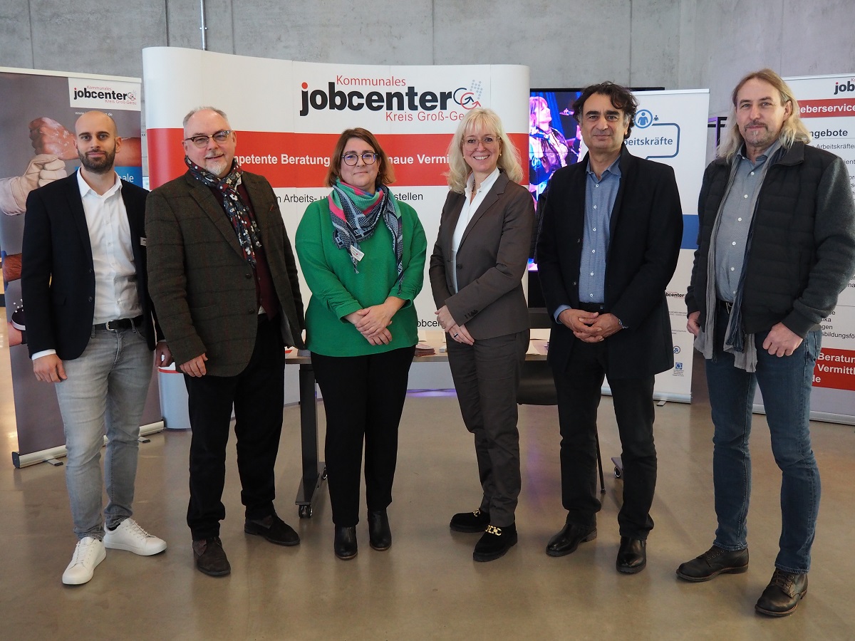 Abbildung sechs Personen vor einer Plakatwand