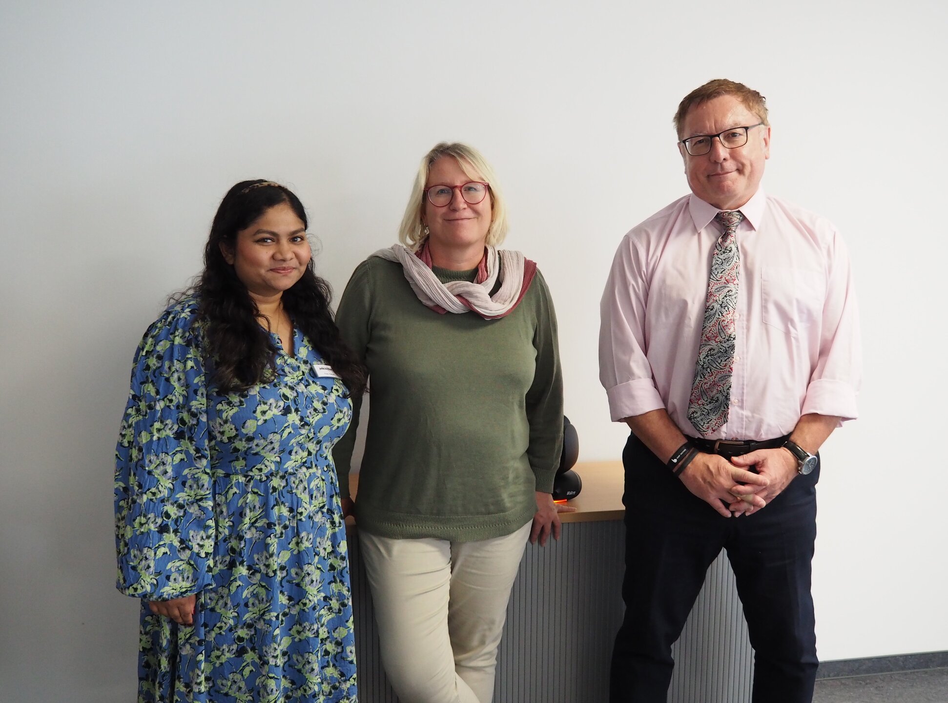 Zwei Frauen und ein Mann stehen vor einer Wand