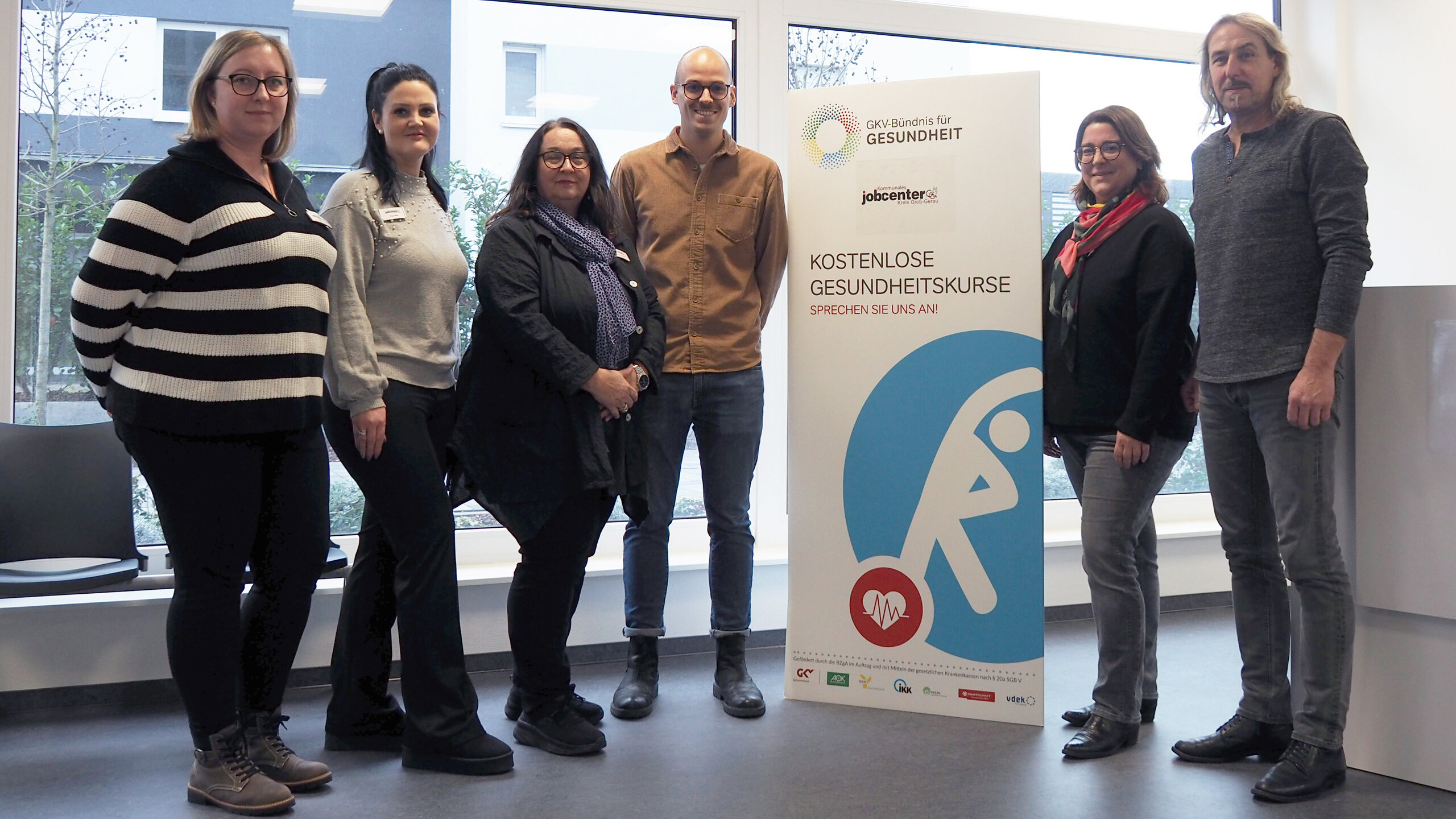 Abbildung sechs Personen neben einem Plakat