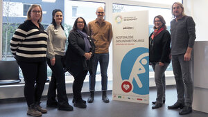 Abbildung sechs Personen neben einem Plakat