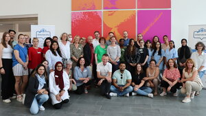 Etwa drei Dutzend Personen stehen und sitzen vor einer Wand